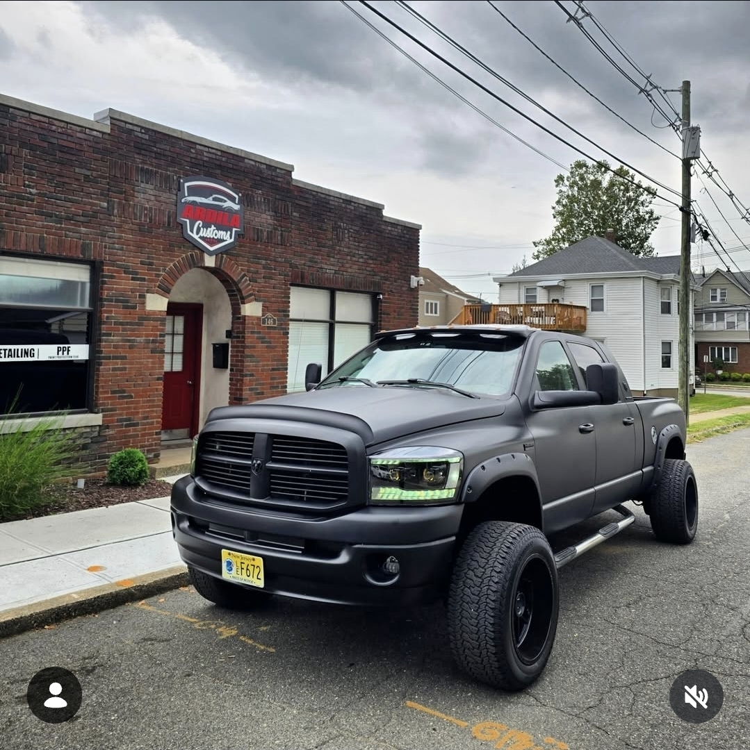 Matte black lifted RAM pickup truck with aftermarket LED headlights outside the shop